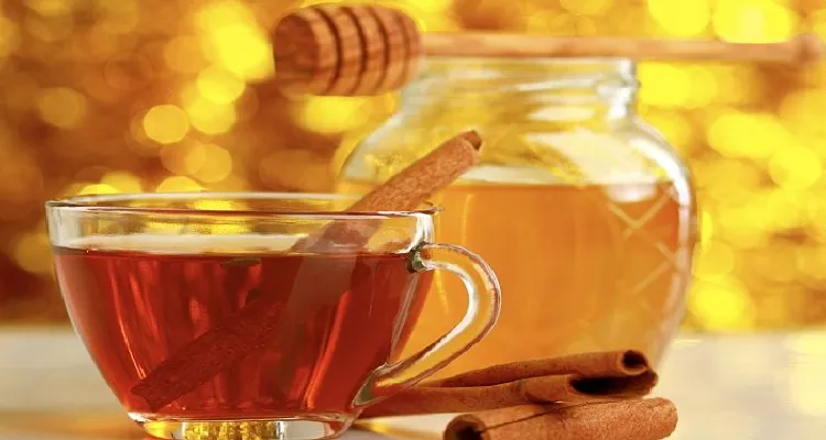 A rustic wooden table with a jar of raw honey, cinnamon sticks, and a warm cup of honey-cinnamon tea in soft sunlight